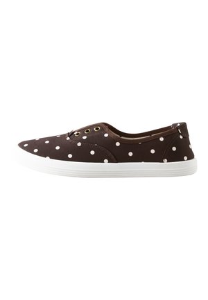 Zapato de lona marrón tipo slip-on con lunares blancos, tres ojales dorados y una suela de goma blanca, mostrado de perfil sobre un fondo blanco.