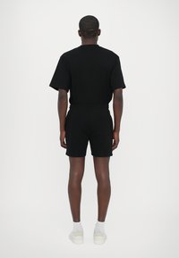 Sort t-shirt med korte ærmer og shorts sæt, lavet af bomuld, med en afslappet pasform. Shortsene har en elastisk talje og går til knæene.