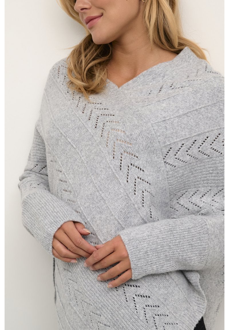 Pelēks adīts džemperis ar V-veida kaklu, ar zigzaga rakstu un ribotām piedurknēm. Mīksta tekstūra un brīva piegriezuma, kas nodrošina ērtu valkāšanu.