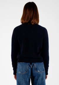 Maglione blu navy con texture e maniche lunghe, caratterizzato da un colletto rotondo e un orlo aderente, abbinato a jeans blu relaxed.