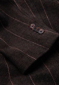 Tessuto a spina di pesce marrone con righe rosa e bianche, caratterizzato da quattro bottoni rotondi marroni con cuciture decorative sul colletto.