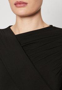 Černý top s volně draped designem a hladkou texturou, s nařasenými detaily po celé tkanině a širokým výstřihem.