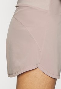 Pantalones cortos deportivos de color rosa claro, elaborados con una tela suave, que presentan un dobladillo curvo y detalles en costuras diagonales para un diseño ajustado.