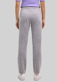 Grijze fleece joggers met een taps toelopende pasvorm, elastische tailleband en geribbelde enkels, gecombineerd met witte sneakers en een lila top.