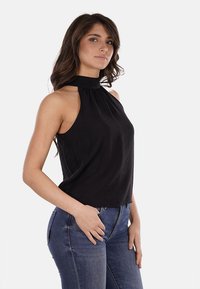 Top nero a collo halter con dettagli plissettati, tessuto leggero, aderente sul seno, silhouette ampia, abbinato a jeans blu.
