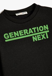 Svart sweatshirt med rund hals, tillverkad av mjukt material, med en grön tryckt grafik "GENERATION NEXT" på framsidan.