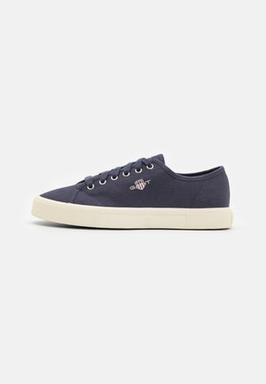 Navy canvas sneakers with beige rubber soles, featuring round laces, metal eyelets, and a small embroidered logo on the side.