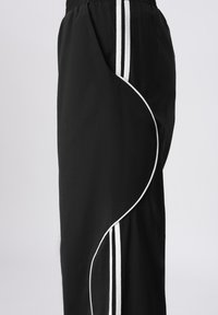 Fekete melegítőnadrág fehér oldalsávokkal és dekoratív fehér pipinggal, lazán szabott, könnyű anyagból.