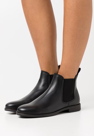 Schwarze Leder-Stiefeletten mit glatter Textur, elastischen seitlichen Einsätzen und flacher Sohle, mit minimalistischem Design und abgerundetem Zehenbereich.