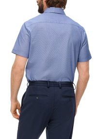 Korte mouwen blauwe shirt met een subtiel ruitpatroon, gecombineerd met marineblauwe broek met achterzakken en knoopaccenten.