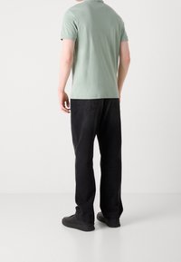 Camiseta de manga corta verde claro con escote redondo, combinada con unos vaqueros negros de corte holgado y zapatillas negras, vista desde atrás.