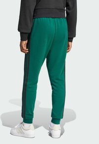 Groene sweatpants met zwarte zijstrepen, een elastische tailleband en enkelmanchetten; gedragen met witte sneakers en een zwart sweatshirt.