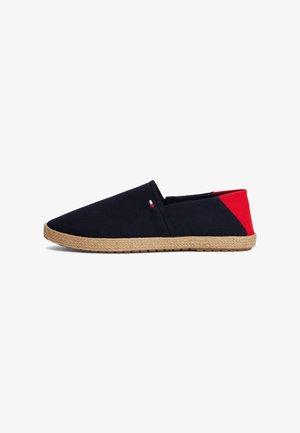 Platna slip-on cipela s gornjim dijelom u tamnoplavoj boji, crvenim naglaskom na peti i jute obrubom. Ima lagani dizajn s ravnim gumenim potplatom.