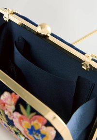 Navy velvet clutch with gold hardware, floral embroidery on the front, and a structured shape; features a slip pocket inside.