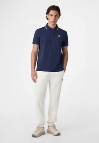 Marinblå pikétröja med krage och kontrasterande röda och vita detaljer. Matchas med krämfärgade mjukisbyxor och beiga sneakers.