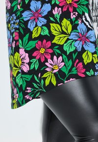 Floral tunic with a black background featuring colorful blue, pink, and green flowers; paired with shiny black leggings.