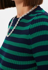 Haut en maille présentant des rayures horizontales bleu marine et vertes, un col rond et une texture côtelée, associé à un collier en chaîne torsadée argentée.