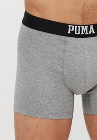 Szürke boxeralsó, puha anyagból, fekete derékkal, amelyen fehér betűkkel szerepel a "PUMA" logó, illeszkedő kialakítással.