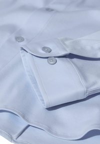 Cămiză bleu deschis cu manșete cu butoni, realizată dintr-un material de bumbac neted. Prezintă butoane asortate și margini cusute cu grijă.