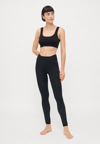 Black athletic top and leggings, both in a smooth, stretchy fabric. The top features a wide strap design, while the leggings have a textured pattern.