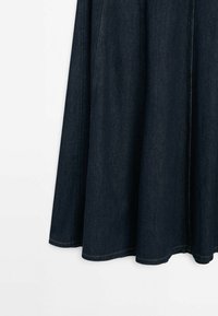 Mörk denimkjol med utsvängd design, med synliga sömmar och en fåll som faller under knäet. Slät textur och klassisk färg.