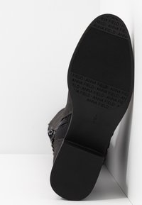 Black ankle boot with a smooth surface, featuring a textured rubber sole, side zip closure, and subtle branding on the sole.