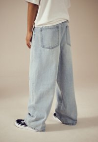 Lyseblå jeans med vide ben lavet af denim, med store baglommer og flosset kant, stylet med sorte sneakers.