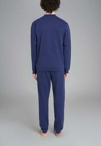 Felpa a maniche lunghe di colore blu navy e pantaloni abbinati realizzati in tessuto morbido. L'outfit presenta un design semplice e una vestibilità comoda senza loghi visibili.