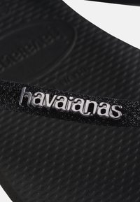 Black textured flip-flop strap with silver "havaianas" logo on the textured sole beneath.