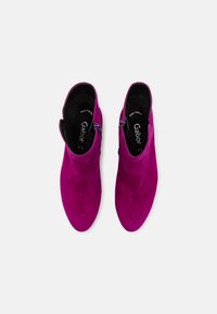 Paire de bottines en daim violet vif avec fermetures éclair latérales, vues de dessus sur un fond clair uni.