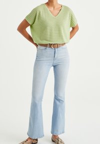 Vihreä neulottu crop-top, jossa on V-kaula-aukko, yhdistettynä vaaleansinisiin leveälahkeisiin farkkuihin ja ruskeaan vyöhön. Kengissä on käärmeennahkakuosi.