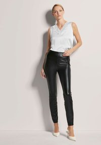 Witte satijnen mouwloze top met een kanten V-hals, gecombineerd met zwarte faux leren strakke broek en wittepuntige hakken. Gladde textuur contrasterend.