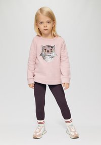 Felpa rosa chiaro con un design di un gufo in paillettes, abbinata a leggings viola scuro e sneakers bianche con accenti rosa e calze a righe.