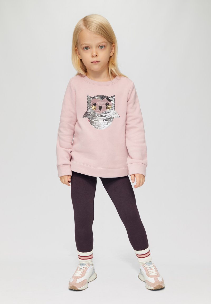 Felpa rosa chiaro con un design di un gufo in paillettes, abbinata a leggings viola scuro e sneakers bianche con accenti rosa e calze a righe.