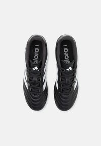Zapatillas de fútbol negras con parte superior sintética, acabado texturizado, tres rayas blancas y cordones negros. Cuenta con una plantilla acolchada para ofrecer soporte.