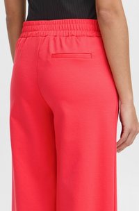 Helle pinke weit geschnittene Hose mit elastischem Bund, aus einem glatten Material und mit einer einzelnen Gesäßtasche.
