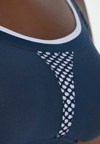 Marineblauwe sportbeha met een witte rand en mesh-details langs het midden. Glad materiaal met een aansluitende pasvorm en gestructureerde naden.