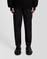 Juodas mezgimo megztinis su deimanto raštu, juodos tiesios kojos džinsai su subtiliu tekstūru, ir masyvūs juodi raištiniai batai.