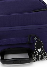Borsa su ruote in tessuto viola con manico nero, tasca con zip e un portachiavi decorativo a forma di scimmia. Texture liscia con cuciture rinforzate.