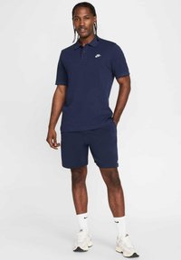 Polo navy de manga corta con un pequeño logo blanco de Nike; combinado con shorts navy. Zapatillas y calcetines blancos completan el atuendo.