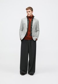 Gray blazer with black accents, ribbed brown turtleneck, and wide black trousers. Model stands straight against a plain background.