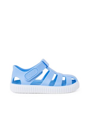 Sandal de goma azul con múltiples tiras, una suela texturizada blanca y hebilla ajustable. Presenta un logotipo en relieve en el costado.