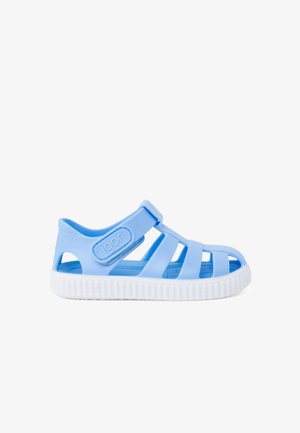 Sandal de goma azul con múltiples tiras, una suela texturizada blanca y hebilla ajustable. Presenta un logotipo en relieve en el costado.