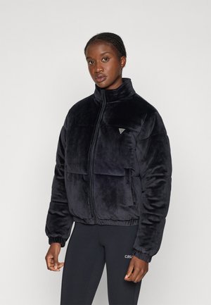 Black plush puffer jacket with a high collar, front zip, and large pockets. Features elastic cuffs and a subtle triangular logo detail.
