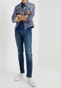 Jeansjacka i ljusblått med vita ränder, i kombination med en marinblå t-shirt med prickar, slim-fit blå jeans och vita sneakers.