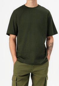 Donkergroene katoenen T-shirt met een klassieke ronde hals, korte mouwen en een relaxte pasvorm, gecombineerd met olijfgroene cargobroek.