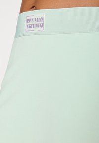 Ljus mintgrön idrottskjol med en texturerad tyg. Midjebandet har en vit etikett med "Tennis Club" i lila bokstäver.