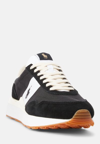 Fekete-fehér sneaker, szövet és suede felső résszel, krémszínű fűzőkkel, narancssárga gumitalppal és kis arany logóval a nyelvén.