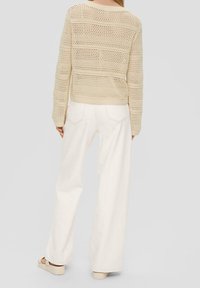 Pull en maille beige avec motif en ajouré et manches longues, associé à un pantalon blanc à jambes larges. Chaussures : sandales plates de couleur claire.