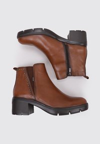 Botas de cuero marrón hasta el tobillo con tacón cuadrado, cierre lateral de cremallera y acentos de tachuelas. Tejido texturizado y suela de goma duradera.